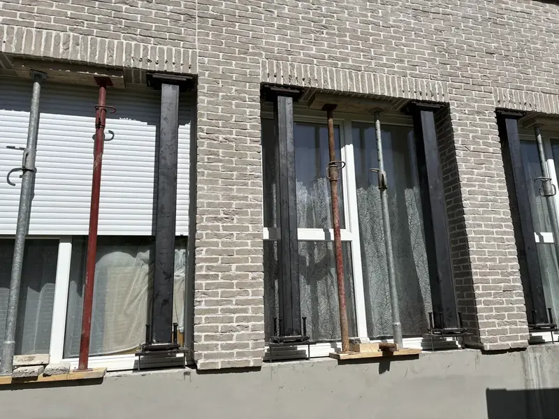 Façade en brique étayée par des étais rouges avant travaux
